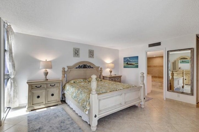 bedroom featuring ensuite bathroom, light tile patterned flooring, and a textured ceiling