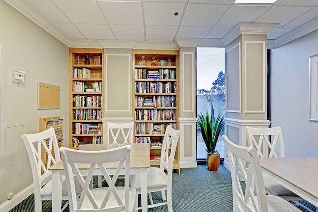 living area with built in shelves, a paneled ceiling, crown molding, and carpet floors