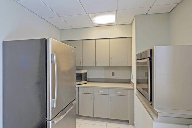 kitchen with appliances with stainless steel finishes, light tile patterned floors, and a drop ceiling