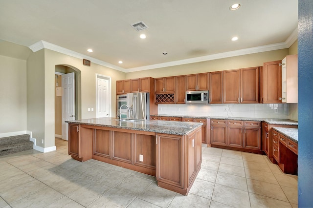 kitchen featuring light stone countertops, appliances with stainless steel finishes, tasteful backsplash, a center island with sink, and light tile patterned flooring