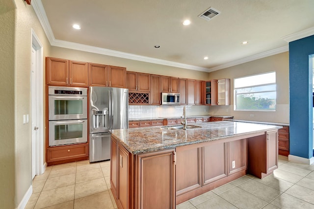 kitchen with sink, stainless steel appliances, light stone counters, and an island with sink