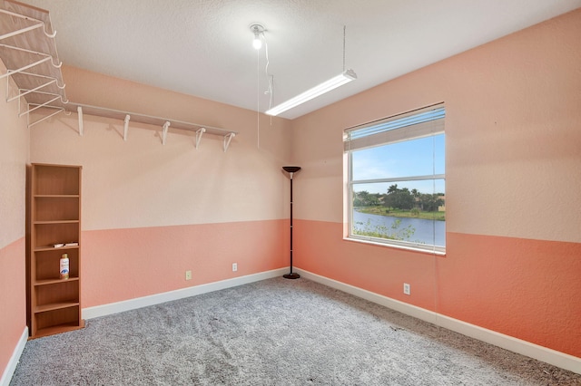 empty room featuring carpet floors, a water view, and a textured ceiling