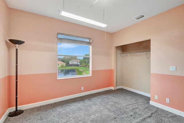 unfurnished bedroom featuring carpet, a water view, and a closet