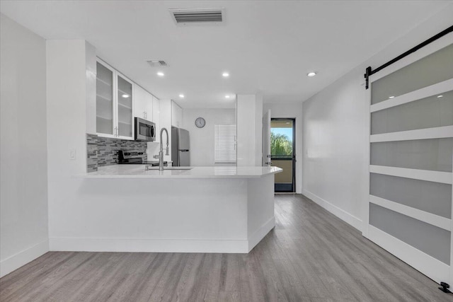 kitchen with kitchen peninsula, stainless steel appliances, a barn door, light hardwood / wood-style flooring, and white cabinets