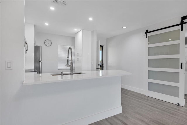 kitchen featuring kitchen peninsula, a barn door, sink, and light hardwood / wood-style floors