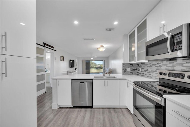 kitchen with kitchen peninsula, a barn door, stainless steel appliances, and white cabinetry