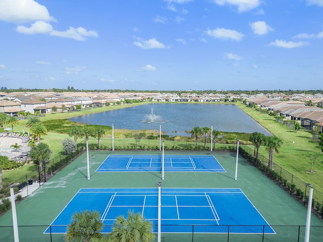 view of tennis court with fence, a residential view, and a water view