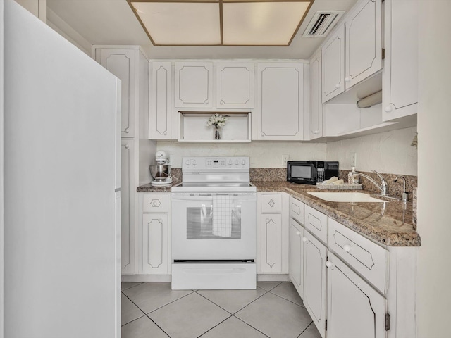 kitchen with white appliances, sink, light tile patterned floors, dark stone countertops, and white cabinetry