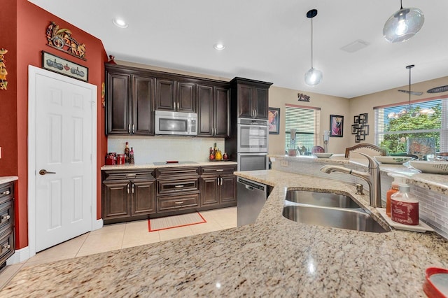 kitchen with appliances with stainless steel finishes, tasteful backsplash, light stone counters, sink, and decorative light fixtures