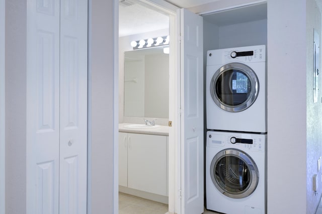 clothes washing area featuring light tile patterned floors, sink, and stacked washer and clothes dryer