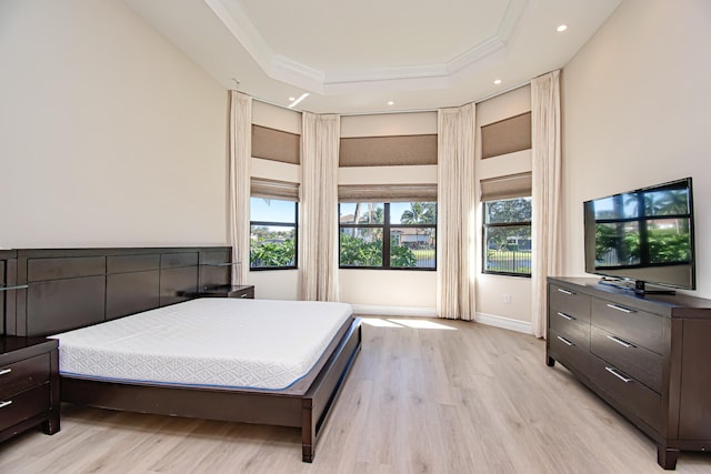 bedroom with ornamental molding, a tray ceiling, multiple windows, and light hardwood / wood-style flooring