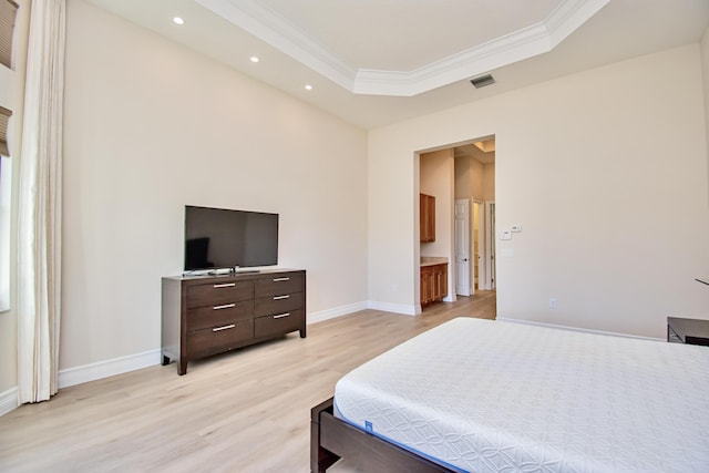 bedroom featuring crown molding, connected bathroom, light wood-type flooring, and a tray ceiling