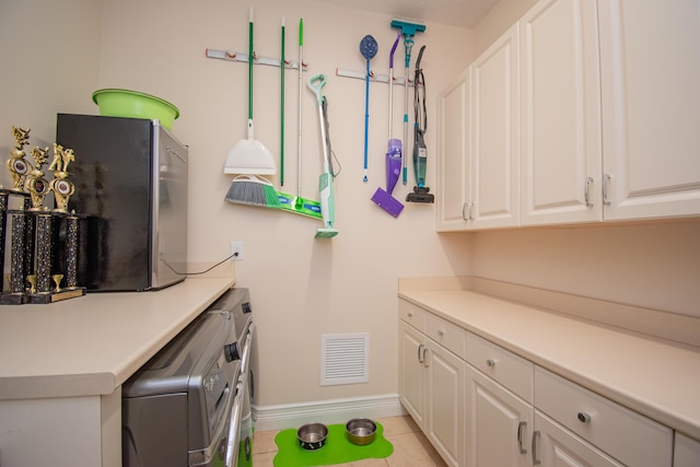 clothes washing area with cabinets, light tile patterned floors, and washer and clothes dryer