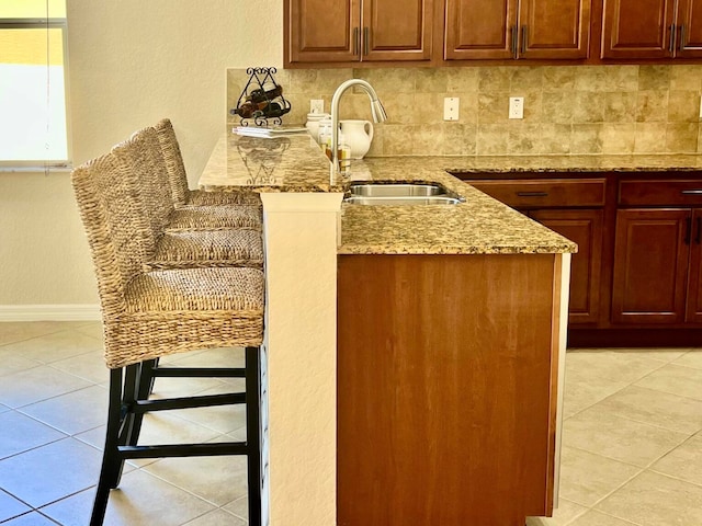 kitchen featuring backsplash, light stone countertops, sink, and a breakfast bar area