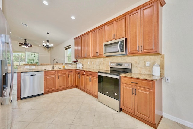 kitchen featuring decorative backsplash, appliances with stainless steel finishes, light stone counters, ceiling fan with notable chandelier, and sink