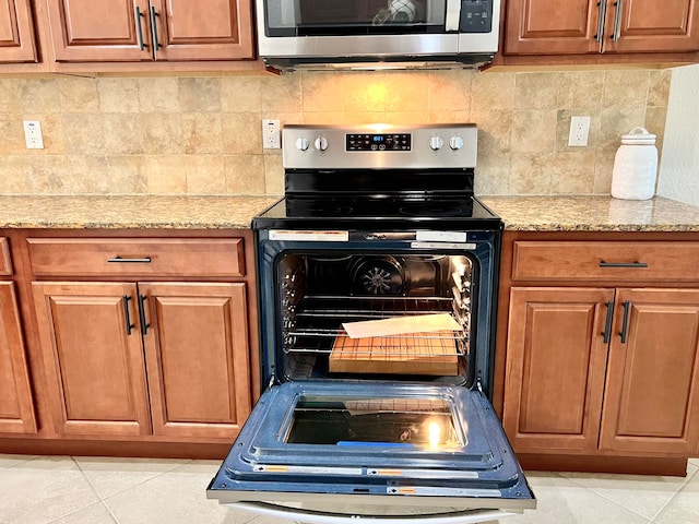 kitchen featuring light stone counters, light tile patterned floors, black range with electric cooktop, and tasteful backsplash