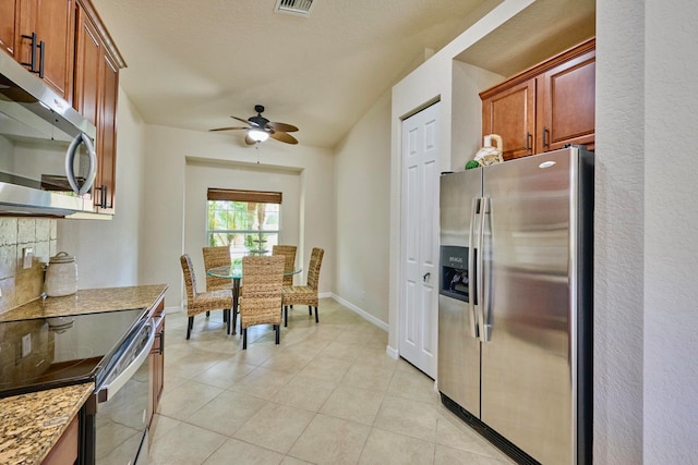 kitchen featuring light stone countertops, light tile patterned floors, stainless steel appliances, and ceiling fan