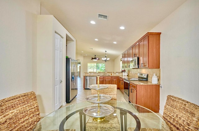 kitchen with an inviting chandelier, light stone countertops, appliances with stainless steel finishes, tasteful backsplash, and kitchen peninsula