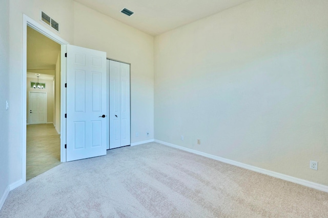 unfurnished bedroom with a closet, light colored carpet, and a notable chandelier