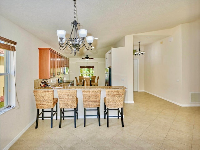 kitchen with stainless steel appliances, kitchen peninsula, a textured ceiling, a kitchen bar, and ceiling fan with notable chandelier