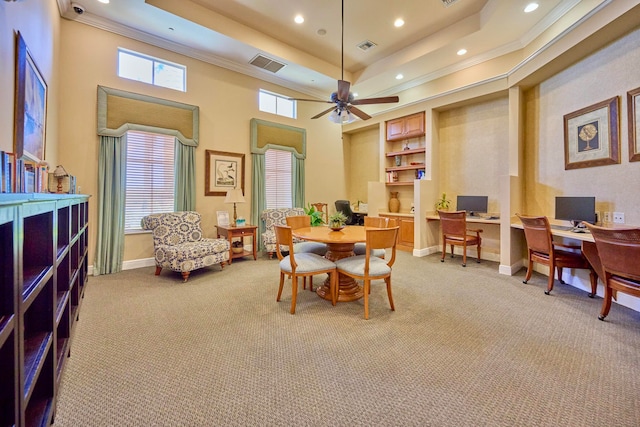 dining area with a towering ceiling, a tray ceiling, light colored carpet, ceiling fan, and crown molding