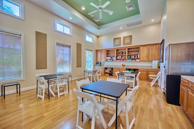 dining room featuring a towering ceiling, light hardwood / wood-style floors, and a healthy amount of sunlight