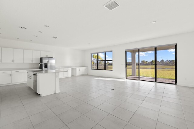 kitchen featuring a kitchen island with sink, light tile patterned flooring, a healthy amount of sunlight, and appliances with stainless steel finishes