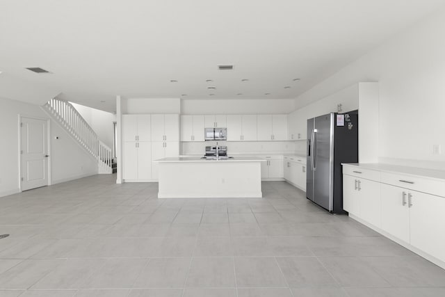 kitchen with white cabinets, appliances with stainless steel finishes, light tile patterned flooring, and an island with sink