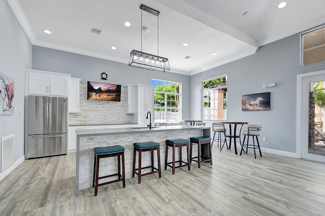 kitchen with a kitchen island with sink, a kitchen breakfast bar, sink, white cabinetry, and stainless steel refrigerator