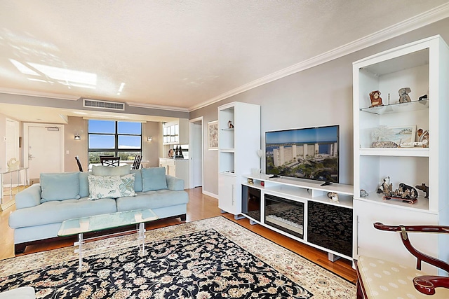 living room with built in shelves, hardwood / wood-style floors, a textured ceiling, and ornamental molding