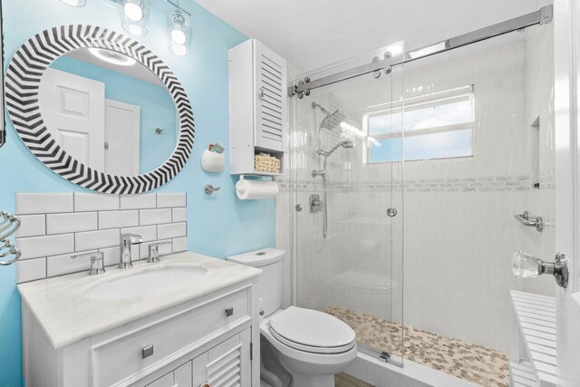 bathroom with toilet, a stall shower, decorative backsplash, and vanity