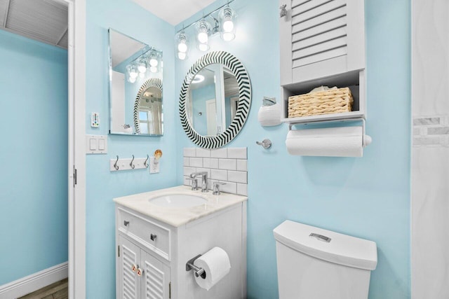 bathroom featuring toilet, baseboards, decorative backsplash, and vanity