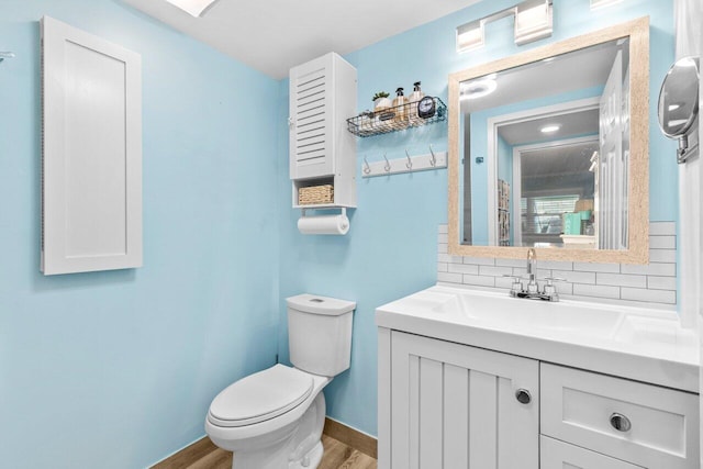 bathroom featuring toilet, decorative backsplash, vanity, wood finished floors, and baseboards