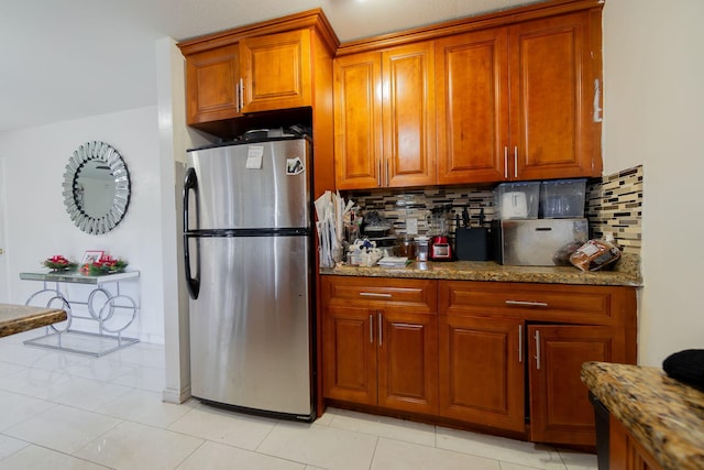 kitchen with stainless steel fridge, light tile patterned flooring, stone counters, and tasteful backsplash