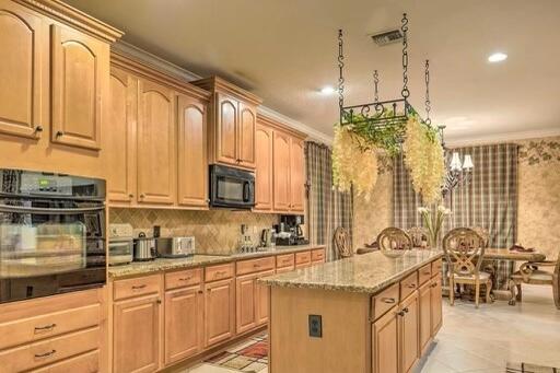 kitchen with light stone countertops, a notable chandelier, crown molding, a kitchen island, and black appliances