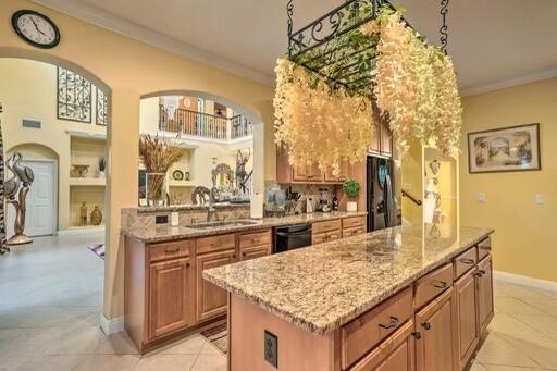 kitchen with light stone counters, crown molding, black appliances, sink, and a center island