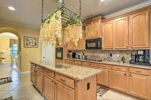 kitchen with a center island, black appliances, crown molding, decorative backsplash, and light tile patterned flooring