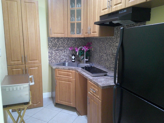 kitchen with black refrigerator, decorative backsplash, sink, light tile patterned floors, and electric cooktop