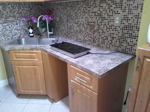 kitchen featuring backsplash, stovetop, light tile patterned floors, and sink