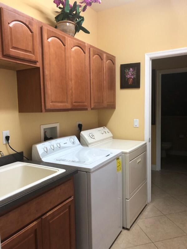 laundry area featuring cabinets, light tile patterned floors, washing machine and dryer, and sink