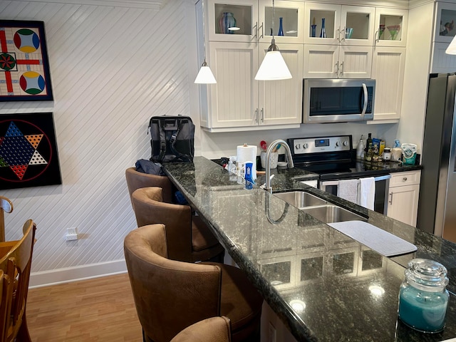 kitchen featuring light hardwood / wood-style flooring, dark stone countertops, decorative light fixtures, white cabinetry, and stainless steel appliances