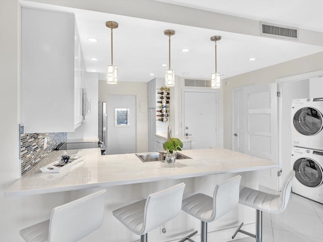 kitchen featuring a breakfast bar, stacked washer and clothes dryer, sink, hanging light fixtures, and kitchen peninsula