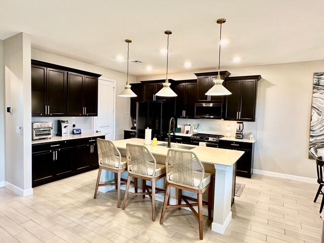 kitchen featuring sink, light hardwood / wood-style flooring, decorative light fixtures, a kitchen island with sink, and appliances with stainless steel finishes