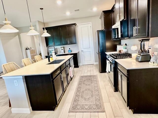 kitchen with hanging light fixtures, an island with sink, stainless steel appliances, and sink