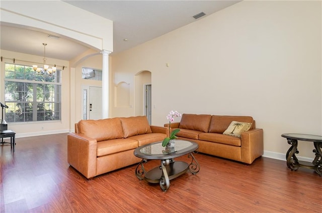 living room with decorative columns, hardwood / wood-style floors, and an inviting chandelier