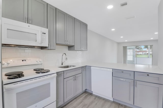 kitchen featuring white appliances, sink, gray cabinets, light wood-type flooring, and kitchen peninsula