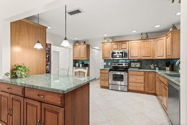 kitchen featuring appliances with stainless steel finishes, backsplash, light stone counters, sink, and hanging light fixtures