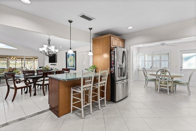 kitchen featuring dark stone counters, ceiling fan with notable chandelier, light tile patterned floors, pendant lighting, and stainless steel fridge with ice dispenser