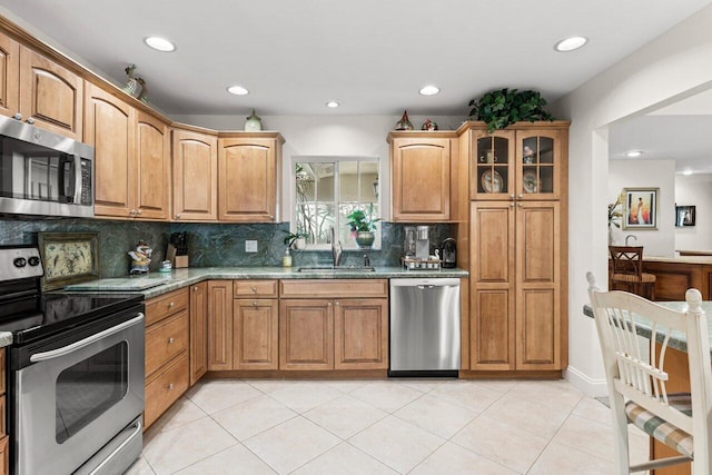 kitchen with appliances with stainless steel finishes, backsplash, light stone counters, sink, and light tile patterned floors