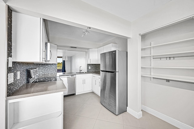 kitchen with sink, decorative backsplash, light tile patterned floors, appliances with stainless steel finishes, and white cabinetry